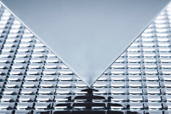 Nahaufnahme einer spiegelnden Metalloberfläche mit einer spitzen Kante, die darauf zeigt. Die Oberfläche hat ein strukturiertes, schuppenartiges Muster.